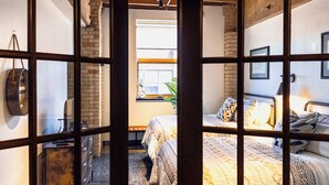 A hotel room with a large window, a bed with patterned bedding, a desk with a chair, and a hanging bag.