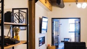 A modern interior with exposed wooden beams, a black sofa, a coffee table, and a bookshelf with decorative items.