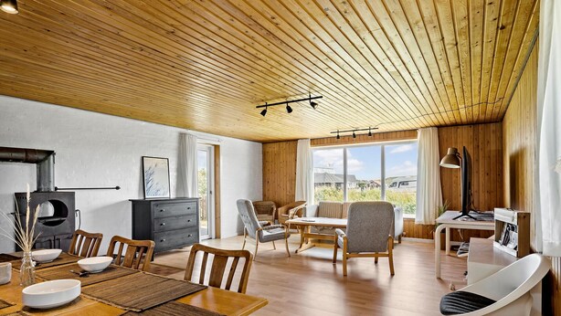 Un salón amplio con techo de madera, una mesa de comedor con sillas, un sofá y un televisor.