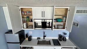 Una cocina compacta con armarios blancos, un microondas integrado y un lavamanos.