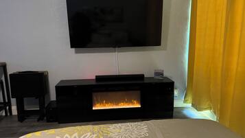 A room with a flat-screen TV mounted on the wall, a fireplace, and a bed with a floral-patterned bedspread.