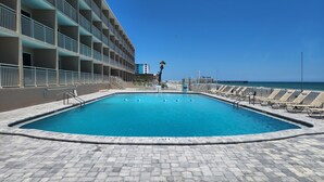 Una piscina con sillones de descanso, cielo despejado y un edificio al fondo.
