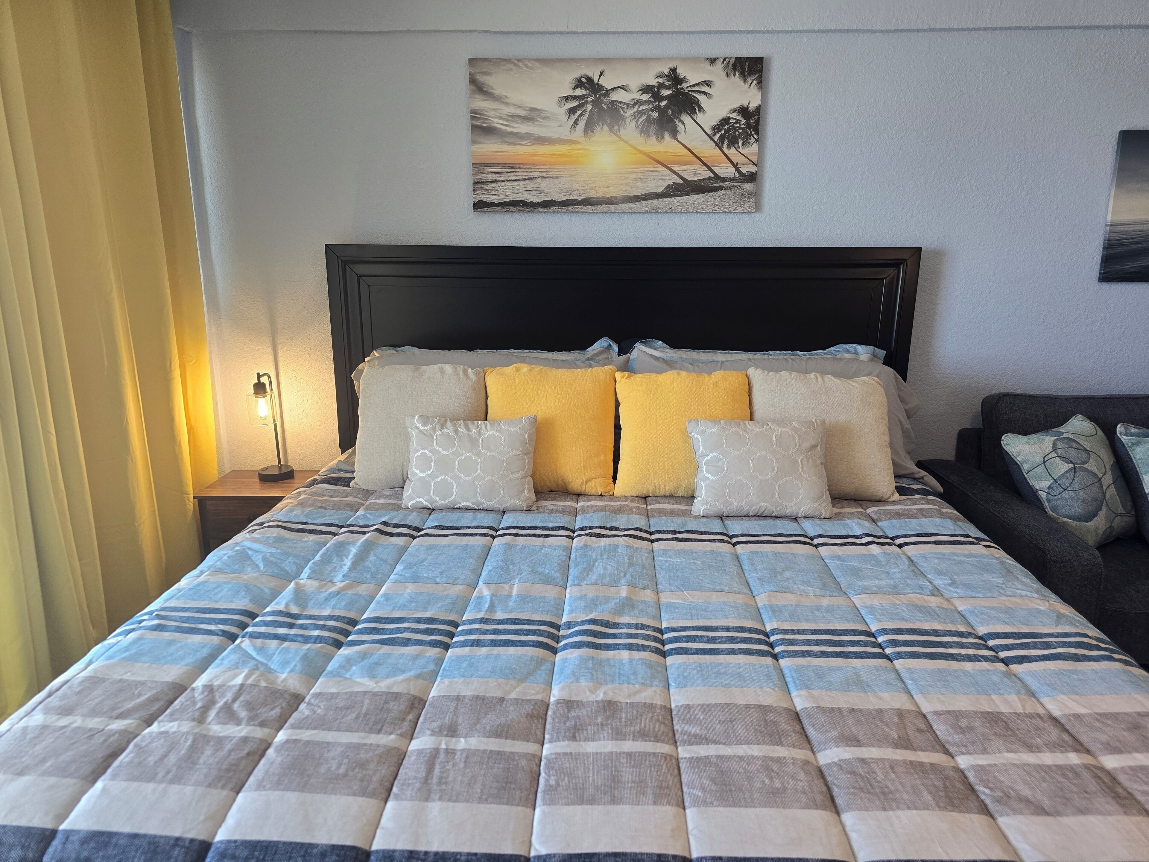 Een keurig opgemaakt bed met een gestreept laken, hoofdbord en meerdere kussens.