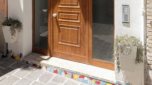 A wooden door with a glass panel, set in a white building with a tiled entrance. - DeA ApartRooms (Termoli)