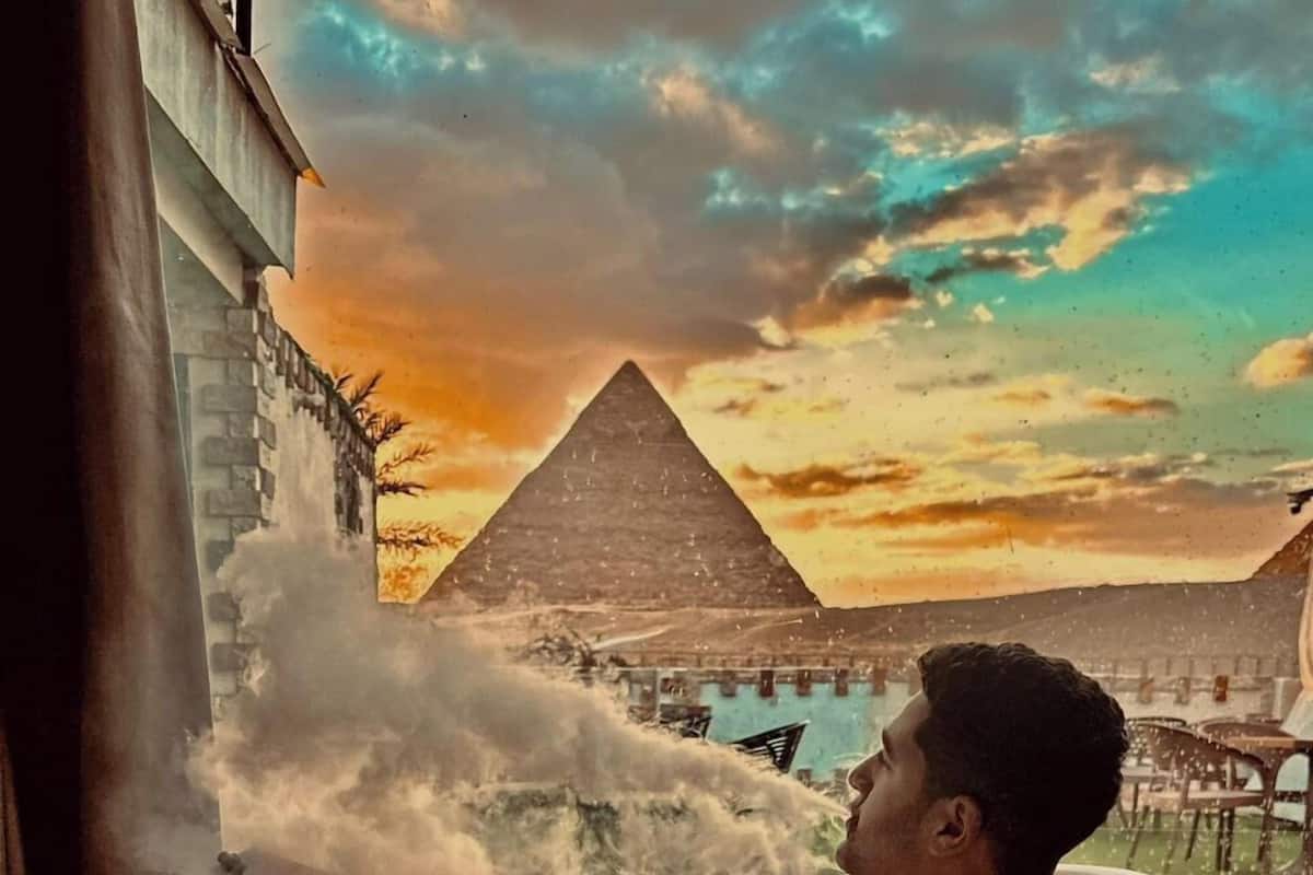 A person relaxing in a large bathtub with a view of a pyramid and a body of water.