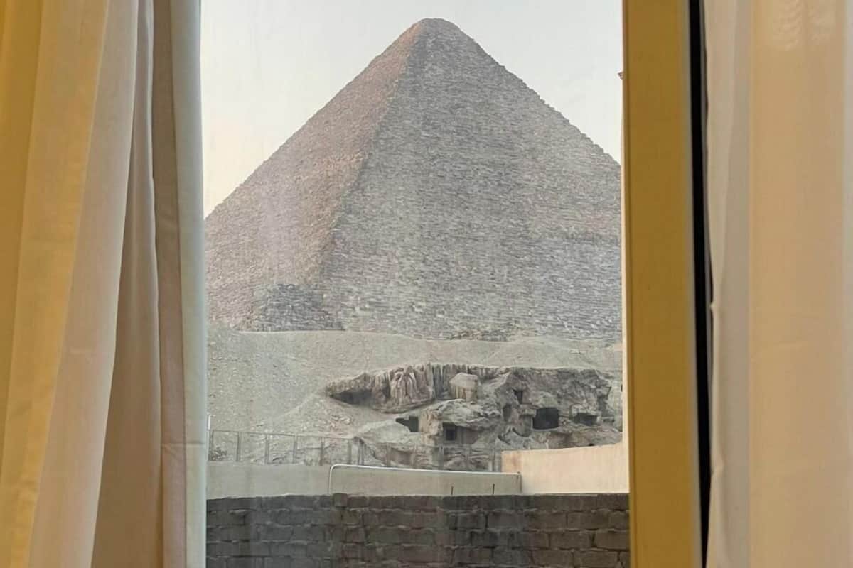 A view of the Great Pyramid of Giza through a window with curtains.