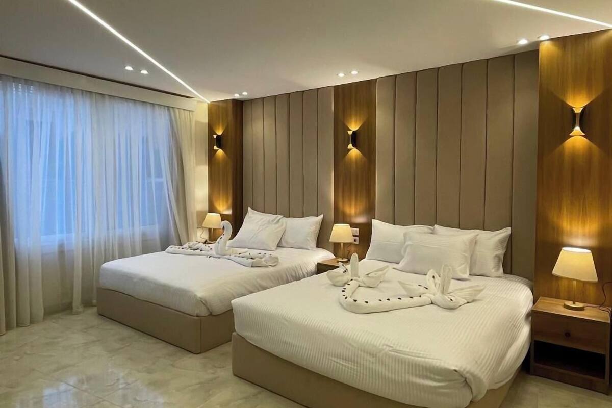 A hotel room with two beds, a large window with sheer curtains, and a marble floor.
