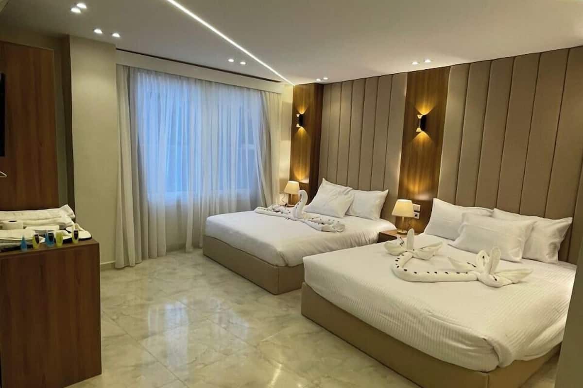 A modern hotel room with two beds, a wooden desk, and a large window with curtains.