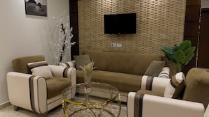 A living room with a brown sofa, two armchairs, a glass coffee table, a wall-mounted TV, and a decorative plant. - White House Pyramids View (Giza)