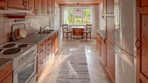 Una cocina con armarios de madera, estufa, refrigerador y un comedor con sillas y mesa.
