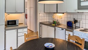 Une cuisine compacte avec des meubles blancs, un four à micro-ondes, un évier et une cuisinière. On y trouve une table à manger en bois avec des chaises.
