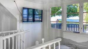 Ein Zimmer mit weißer Geländer, einem Bett mit gestreifter Bettwäsche, einem Gemälde an der Wand und Blick auf einen Steg und Wasser.