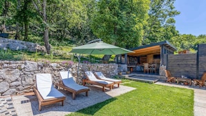 A patio with lounge chairs and a stone wall, a wooden deck, and a stone building with a covered outdoor area.