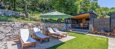 Un patio con sillones de descanso y un muro de piedra, una terraza de madera y un edificio de piedra con un área al aire libre cubierta.