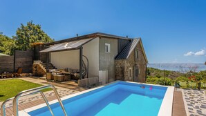 A pool area with a clear view of the sea, a covered outdoor seating area, and a stone building.