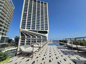 Un hotel moderno con zona de piscina, destacando un diseño arquitectónico único con balcón curvo y sillones de descanso.