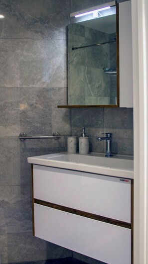 Un baño con pared de mármol, un lavamanos blanco con dispensador de jabón y un espejo sobre el lavamanos.