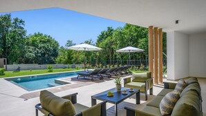 Un espace aménagé au bord de la piscine, avec des chaises longues, des parasols et une table agrémentée d’une plante en pot.