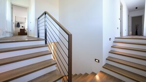 Un escalier moderne avec des marches en bois et une rampe en métal, menant à une pièce lumineuse aux murs blancs et au plancher en bois.