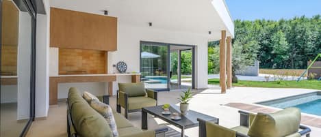 Un espace de vie extérieur moderne comprenant une piscine, des sièges et un barbecue.