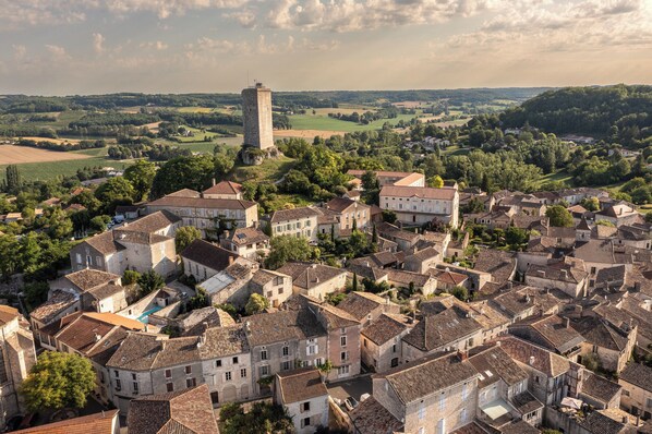 Un pueblo histórico con edificios de piedra, una torre destacada y campos circundantes.