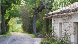 Un bâtiment rustique en pierre, doté d’un toit en tuiles, entouré d’une végétation luxuriante et d’arbres.