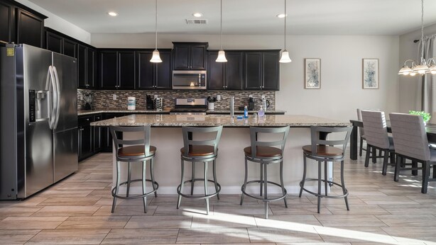 Une cuisine moderne avec des meubles de couleur sombre, des appareils en acier inoxydable et un îlot central doté de tabourets de bar.