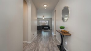 Un couloir doté d’un plancher en bois, d’un miroir rond accroché au mur et d’une petite table sur laquelle est posée une plante.