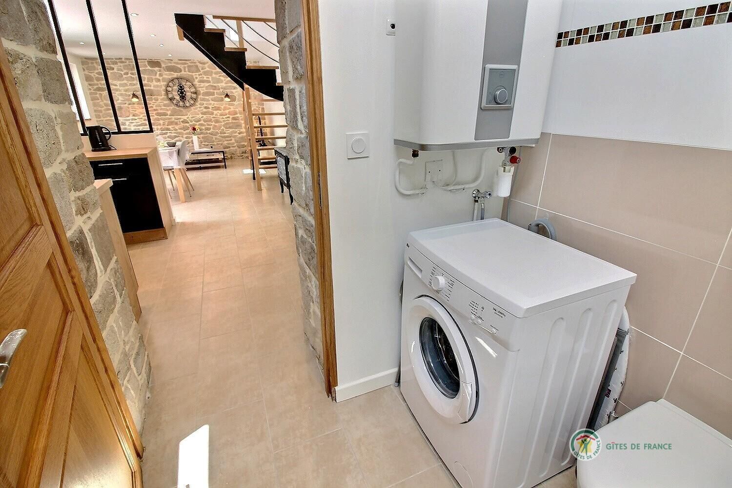 A laundry room with a washing machine, a small sink, and a tiled wall.