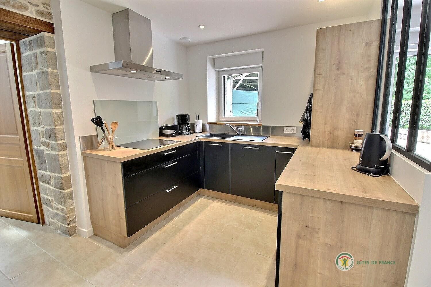 A modern kitchen with black cabinets, a stainless steel range hood, a window, and a coffee maker.
