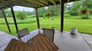 Eine überdachte Terrasse mit Holztisch und -stühlen, Topfpflanzen und Blick auf eine Rasenfläche.