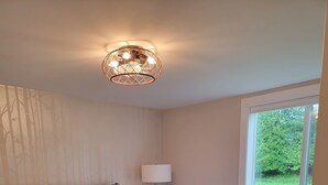 Ein Schlafzimmer mit einem hölzernen Bett, einem Nachttisch mit Lampe, einem Fenster mit Blick auf Grünflächen und einer Wand mit Baumstruktur.