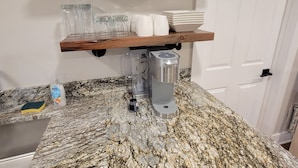 Eine Küche mit Granit-Arbeitsplatten, einer Kaffeemaschine und Gläsern in Regalen.
