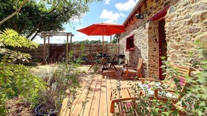 A rustic outdoor patio with wooden furniture and a red umbrella, surrounded by stone walls and greenery. - De Rulinen - Orchard side (SAINT CLET)