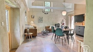 A spacious living area with a high ceiling, a dining table with chairs, a sofa, and a TV. - De Rulinen - Orchard side (SAINT CLET)