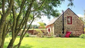 A stone building with a red window and a chimney, surrounded by trees and a grassy area. - De Rulinen - Orchard side (SAINT CLET)