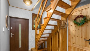 Una escalera de madera que conduce a un piso superior, una puerta de madera con un espejo y una corona en la pared.
