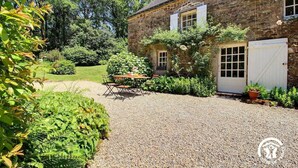 Un bâtiment en pierre avec une allée gravillonnée, une table en bois avec des chaises et une porte blanche.