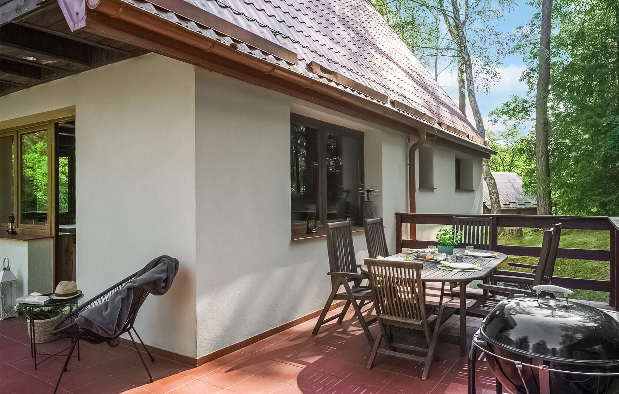 Une terrasse avec une table et des chaises, un barbecue et une vue sur la verdure environnante.