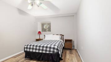 A bedroom with a bed, a nightstand, a lamp, a ceiling fan, and a window.