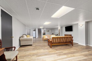 Un salón espacioso con suelo de madera, un sofá, una silla y un televisor montado en la pared.