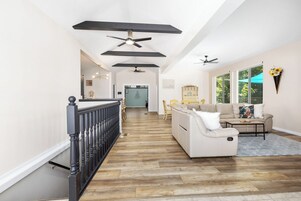 Un salón amplio con suelo de madera, un sofá blanco, una mesita de centro y un ventilador de techo.