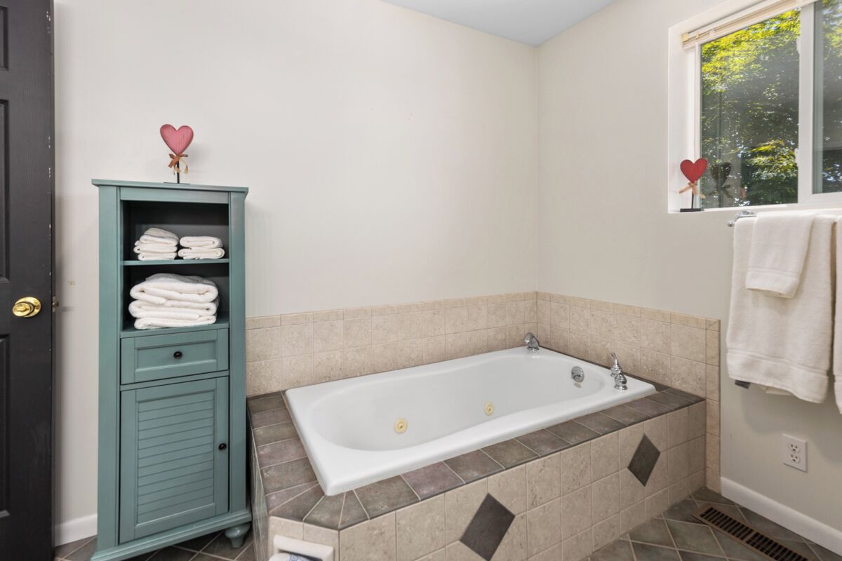 A bathroom with a bathtub, a green cabinet with towels, and a window with a view of trees.