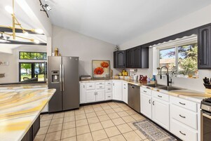 Una cocina moderna con armarios blancos, un refrigerador de acero inoxidable, horno empotrado y un amplio ventanal que proporciona luz natural.