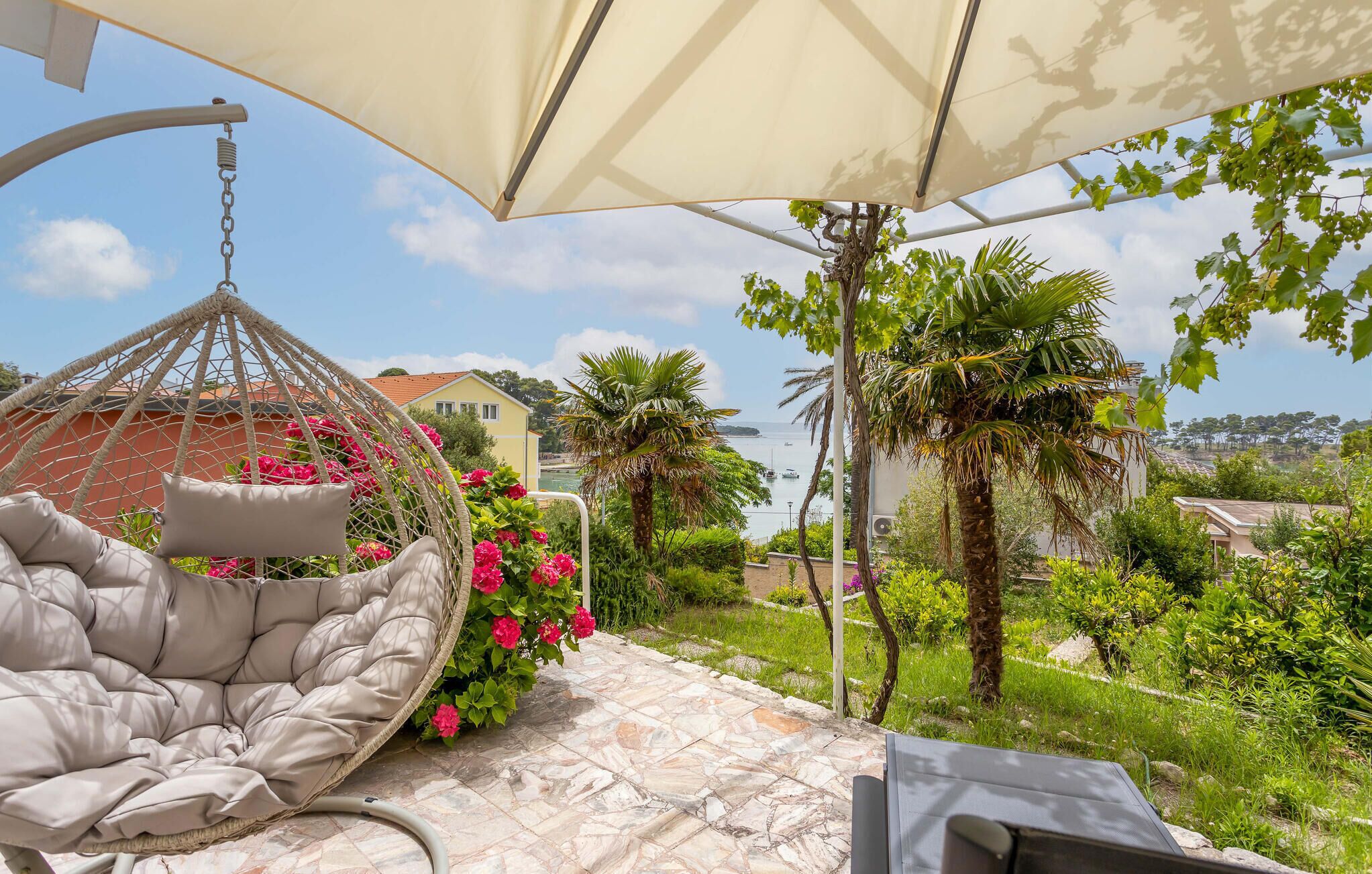 A hanging chair with cushions, a stone patio, and a view of the sea and buildings.