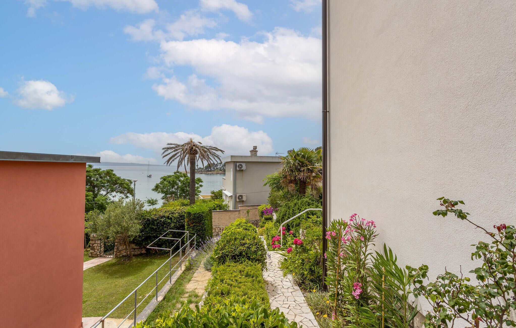 A garden with a pathway, palm trees, and a view of the sea.