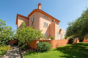 A two-story building with a garden pathway, outdoor seating, and a clear sky.