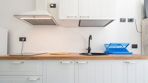 Una cocina con armarios blancos, encimera de madera, grifo negro y escurreplatos azul.