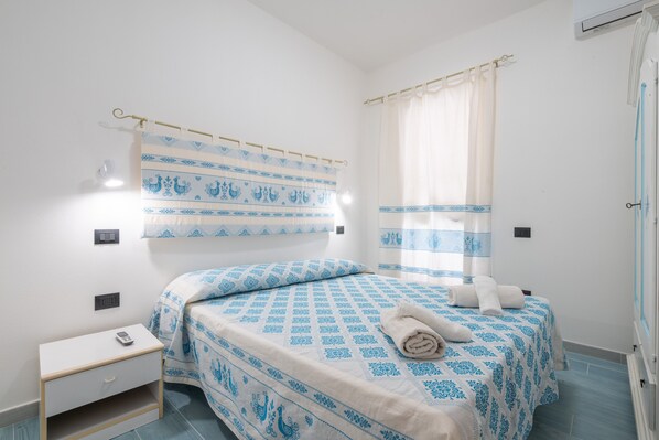 Un dormitorio con una cama, una mesita de noche, una cortina y una lámpara fijada a la pared.