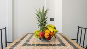 Una mesa de comedor con un frutero que contiene piña, plátanos, uvas y naranjas.
